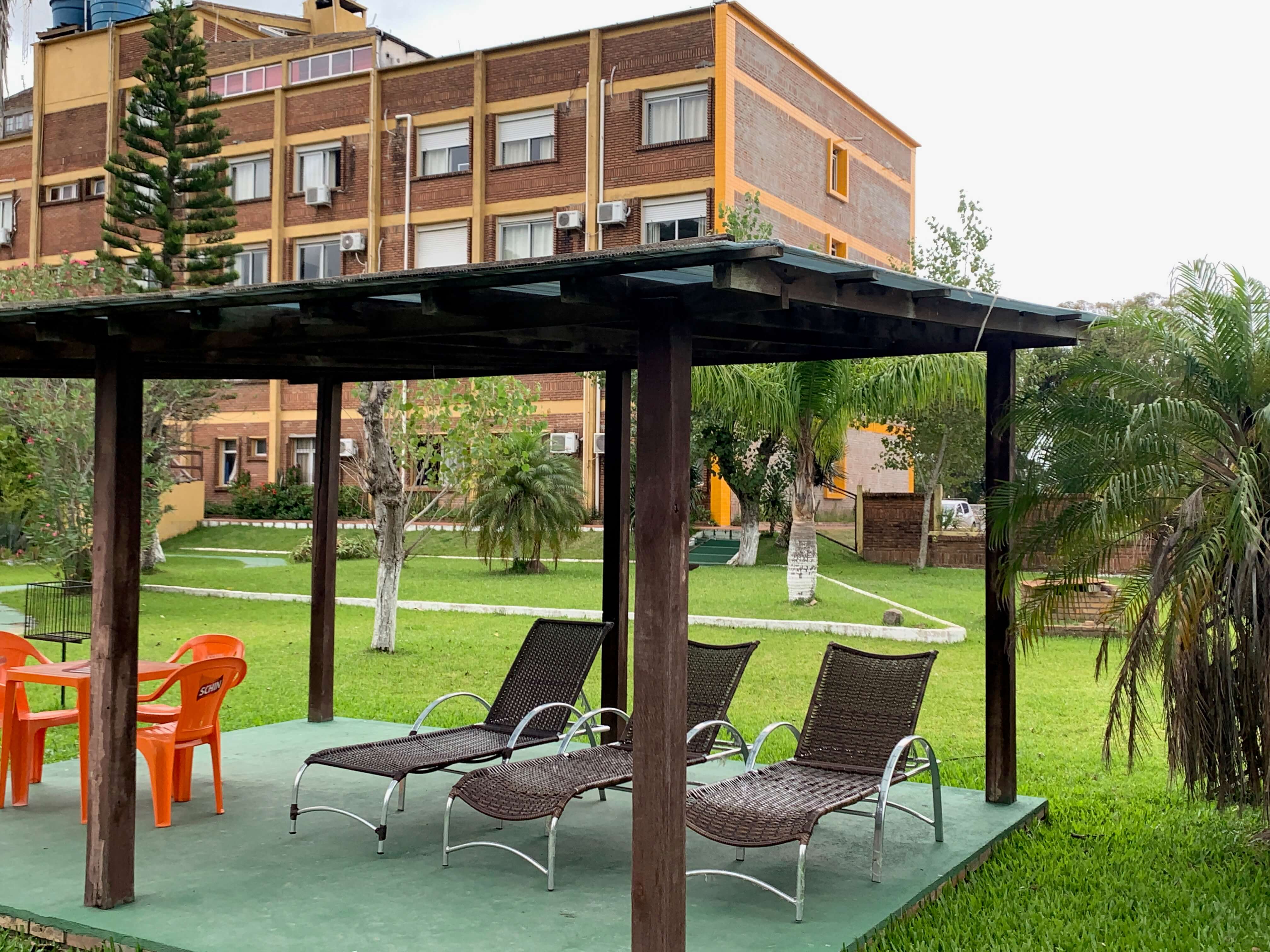 Parte externa do hotel Bertelli, com pergolado, cadeiras, árvores e área verde
