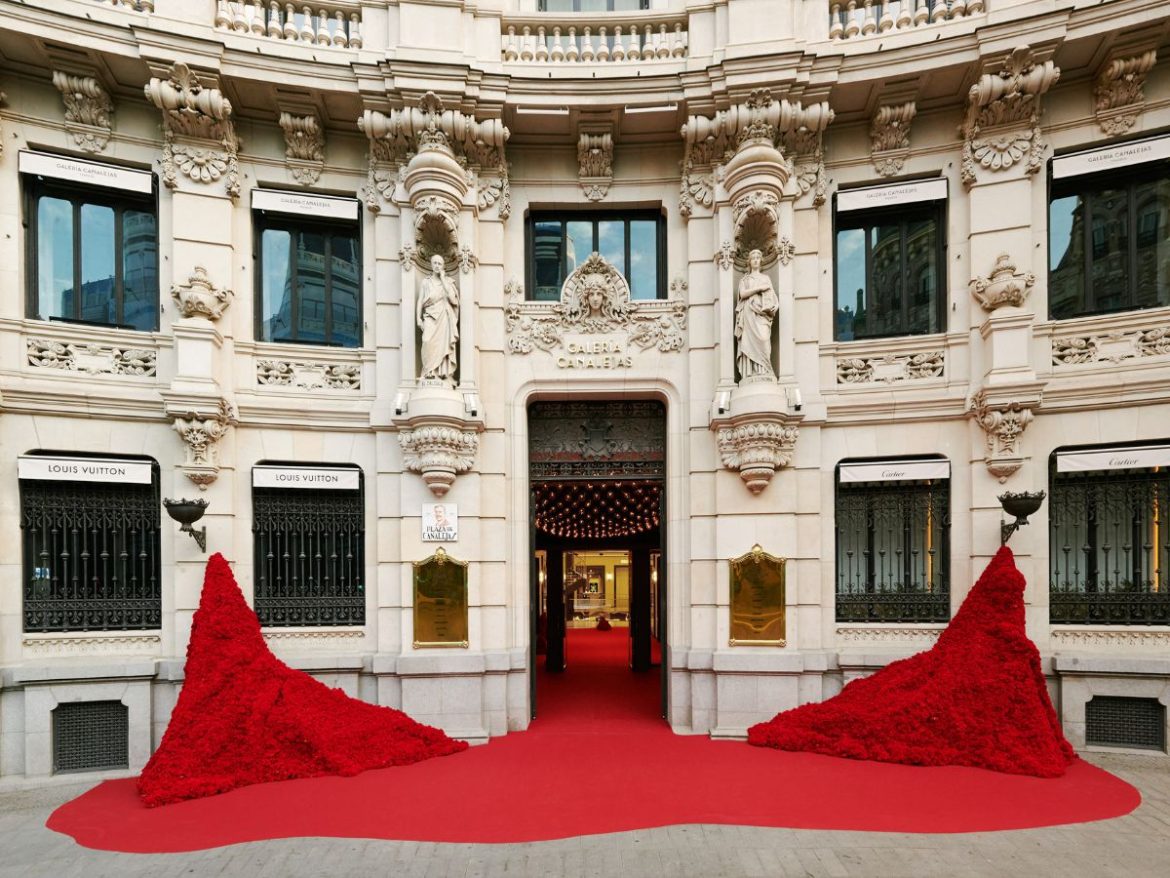 O que fazer em Madri: na foto aparece a fachada de um antigo prédio espanhol restaurado, coberta de cravos vermelhos, que vão das paredes ao chão, acompanhando um tapete que segue para dentro da galeria canalejas